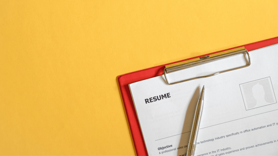 Red clipboard on a yellow background with a Resume clipped to the front